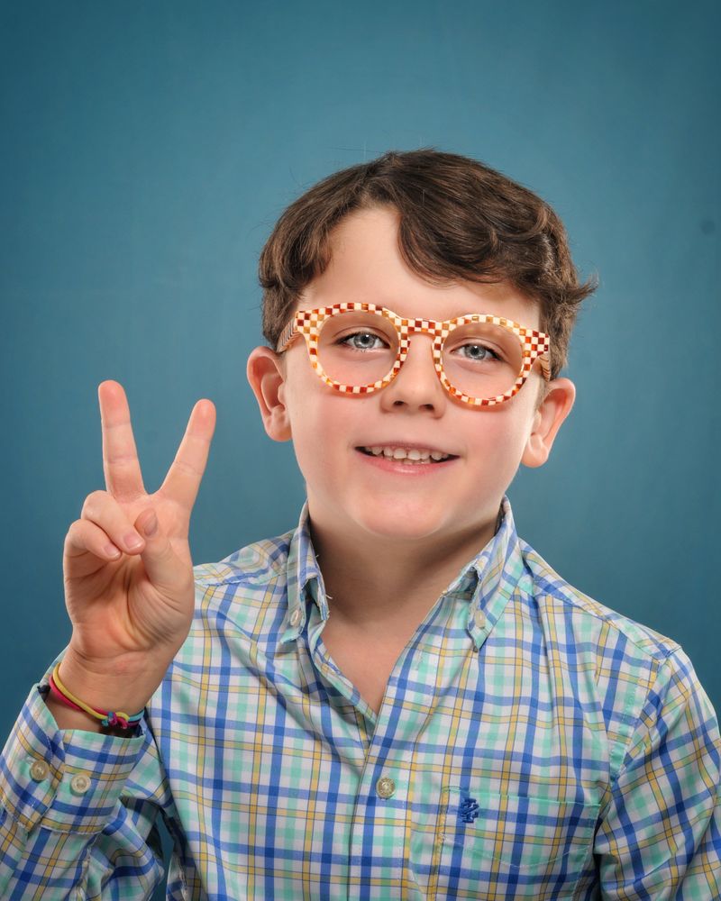 A young patient in orange checkered glasses giving a peace sign
