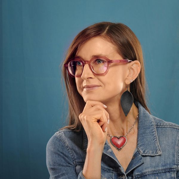A patient of The Optical Centre in a jean jacket and heart necklace, wearing pink frames